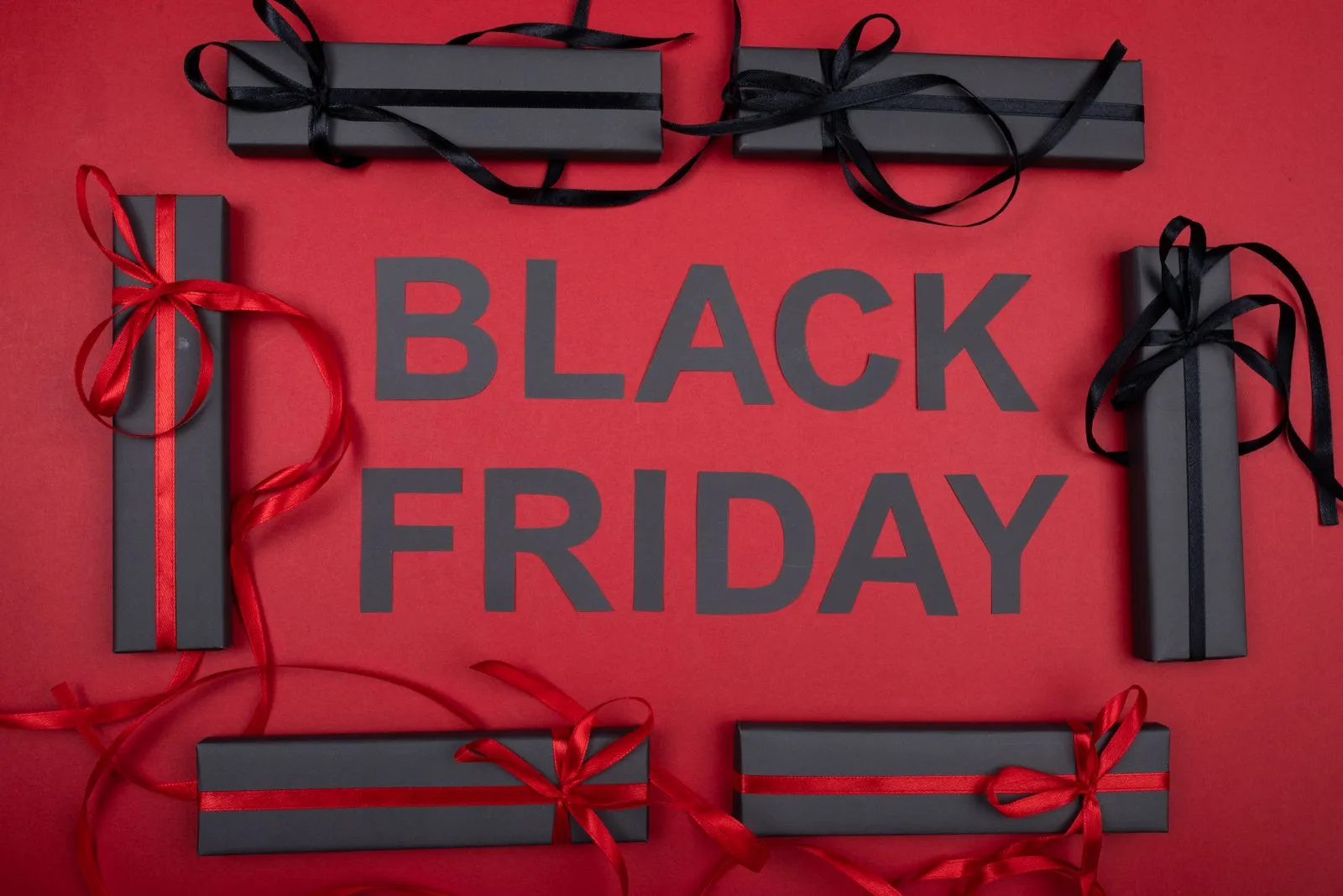 Black gift boxes and ribbons around Black Friday lettering on a red background