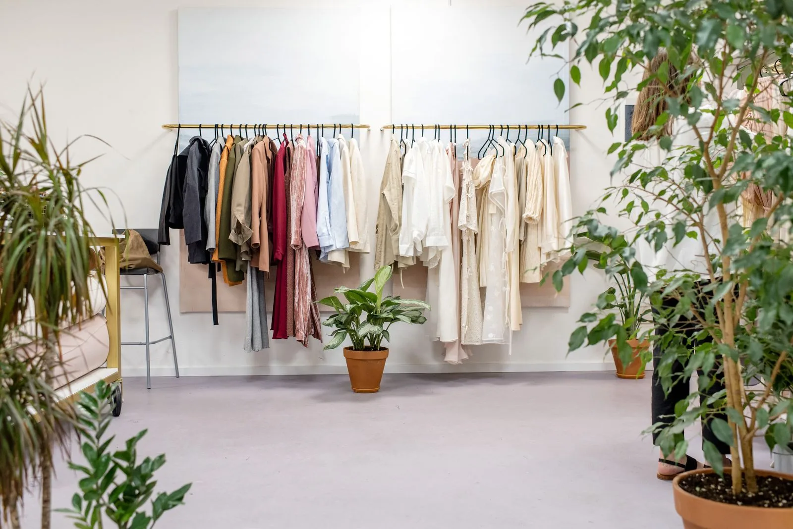 Clothes on hangers along two wall rails in a bright boutique with potted plants