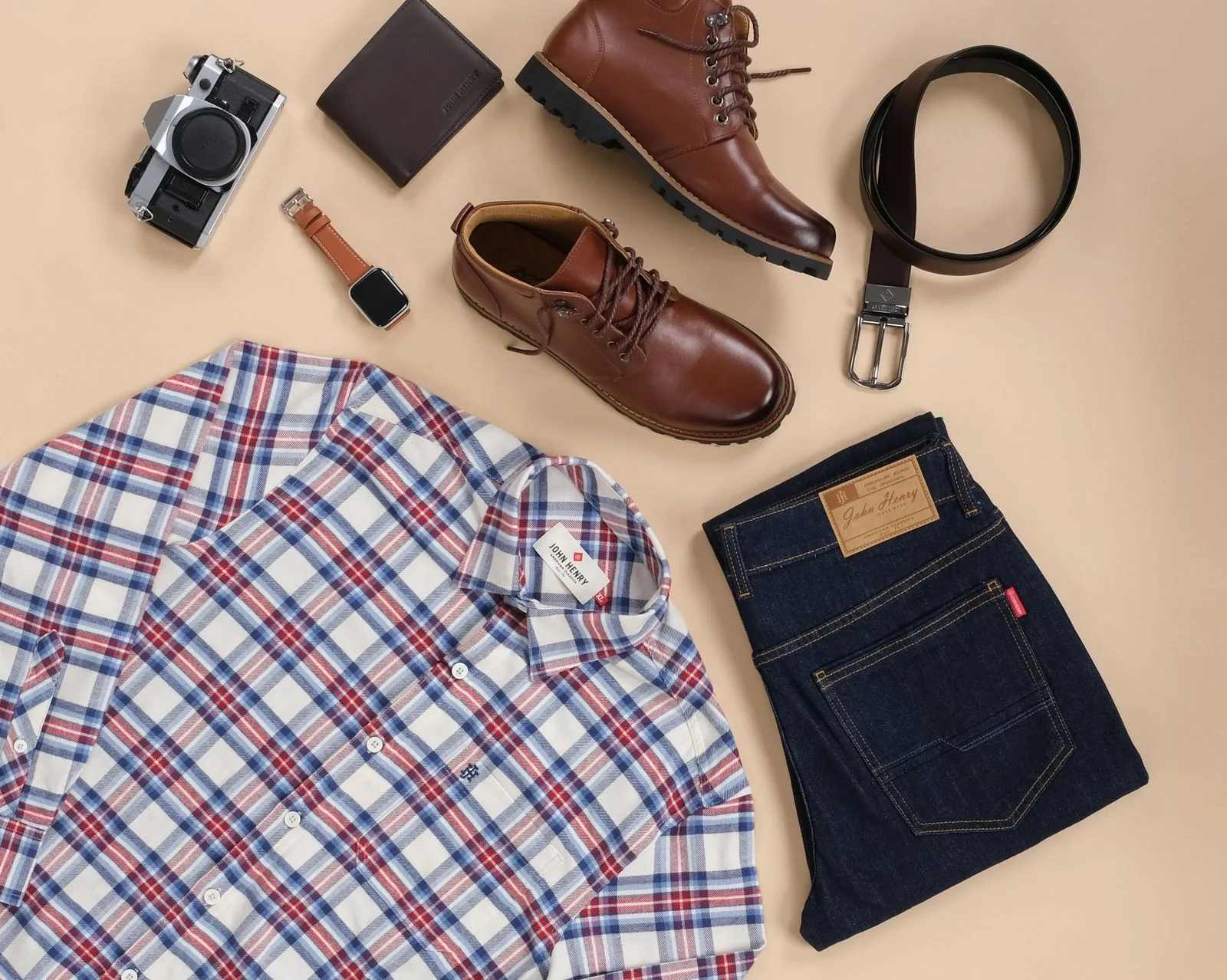 Plaid shirt, dark jeans, brown boots, a belt, a watch, a wallet, and a camera arranged on a beige background